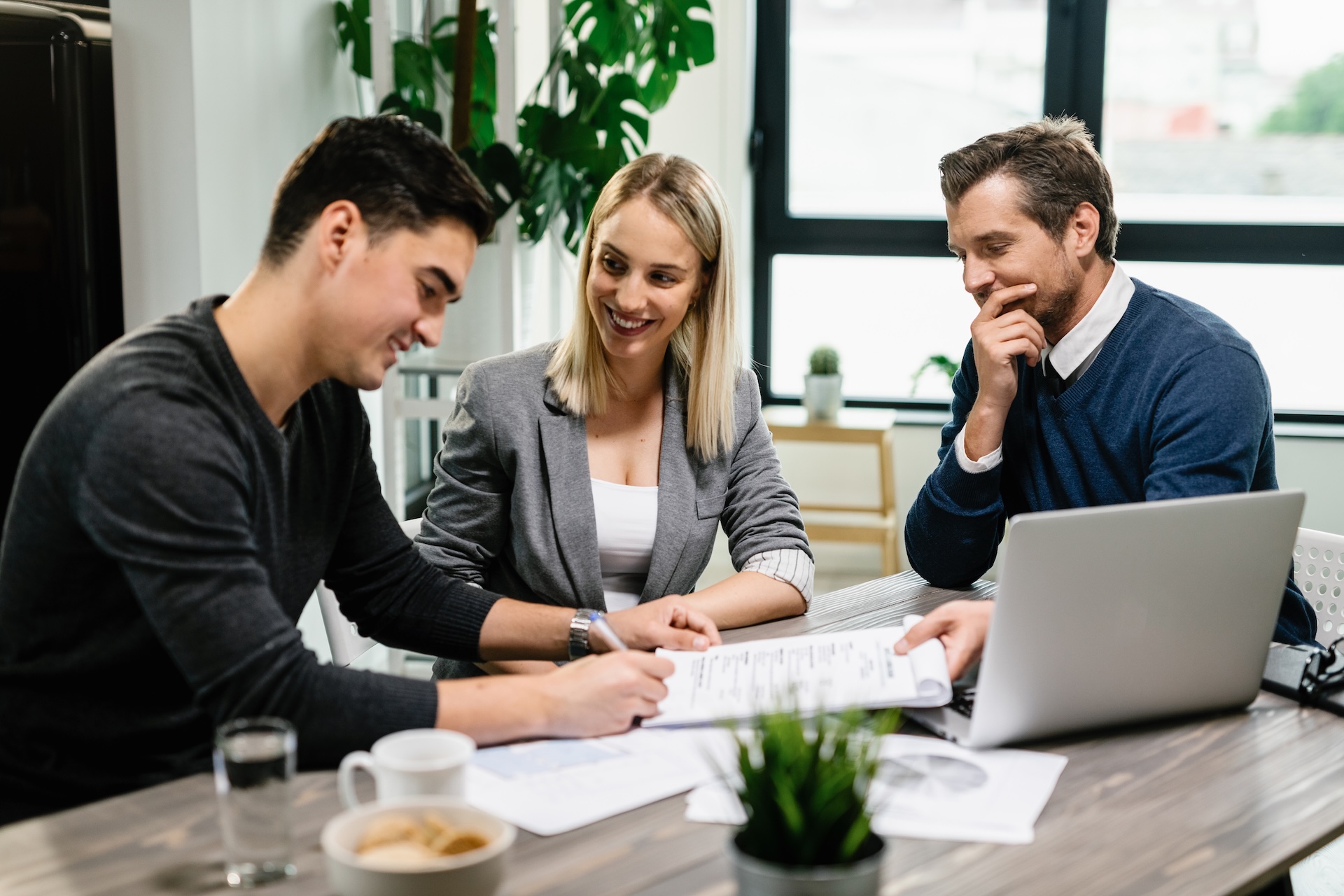 Three business professionals sitting at a table smiling and reviewing documents together.