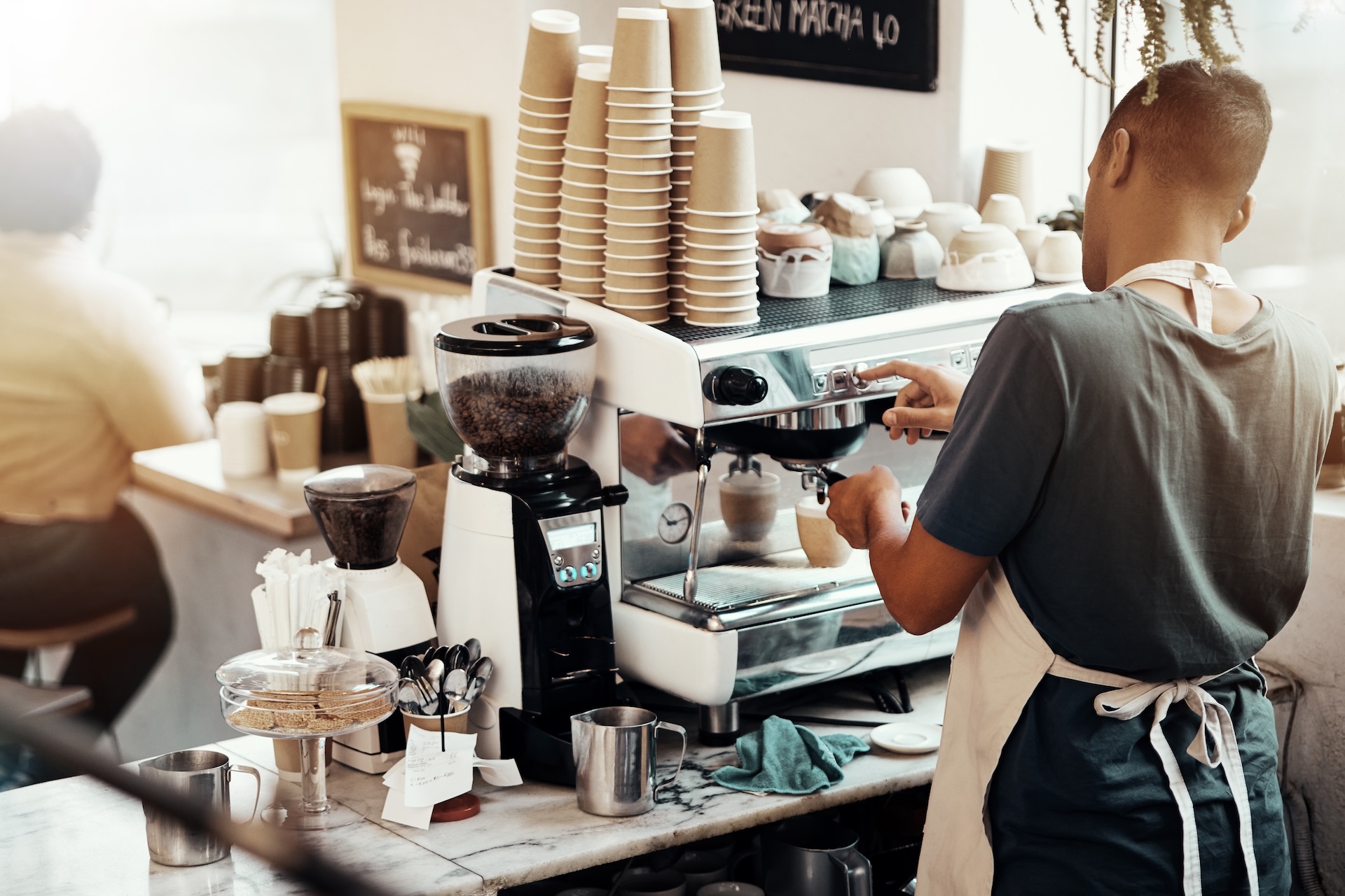 Barista operating a commercial espresso machine in a cozy coffee shop.